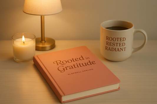 generate an image with a journal called Rooted in Gratitude by BEWEll Darling. This journal is a soft coral color. place this journal on a desk with a lamp , coffe mug that says Rooted rested radiant. add candle